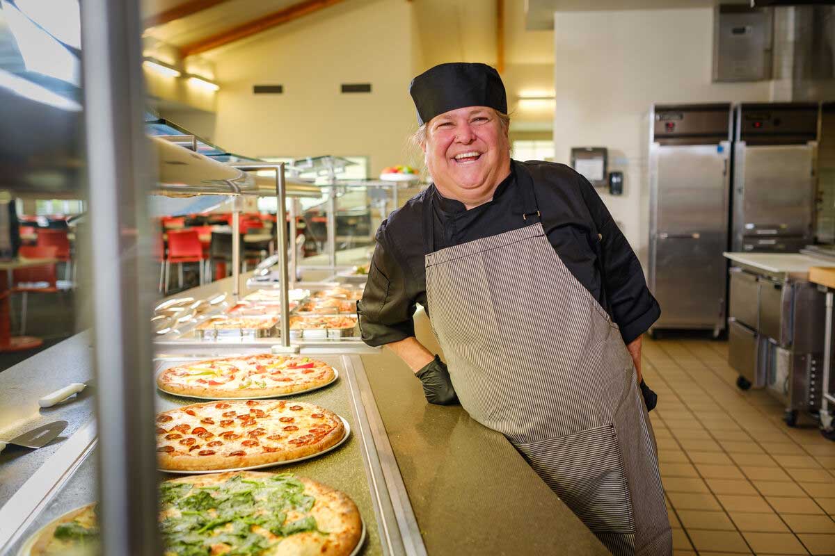 Cook smiling behind pizza station line